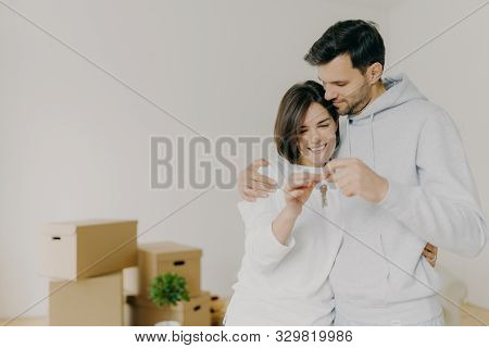 Delighted Woman And Man Home Owners Enjoy Buying New Flat, Hold Keys Fromm Their Own Apartment, Pose