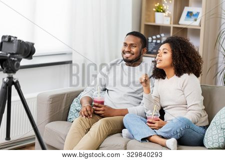blogging, videoblog and people concept - happy african american couple of video bloggers with camera and smoothie drinks videoblogging at home