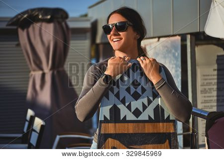 Brunette Girl In Gray Turtleneck, Denim Shorts And Sunglasses Is Posing With Her Wakeboard Satnding 