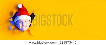 Little Cheerful Santa In A Hat Smiles, Getting Out Of The Ragged Yellow Background Lit By Neon Light