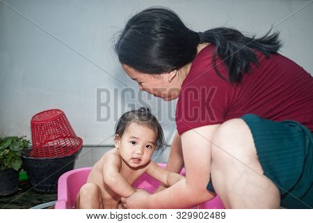 Asian Woman Washing Her Daughter In Bathtub, Baby Girl Taking A Bath In Pink Tub