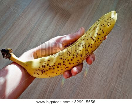 A Ripe Banana In The Hand With Wooden Background.