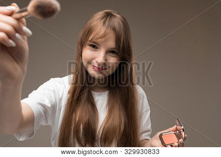 A Young Beautiful Girl With Long Wavy Rustic Hair, Nud Makeup, Wearing A White Jersey, Holds A Makeu