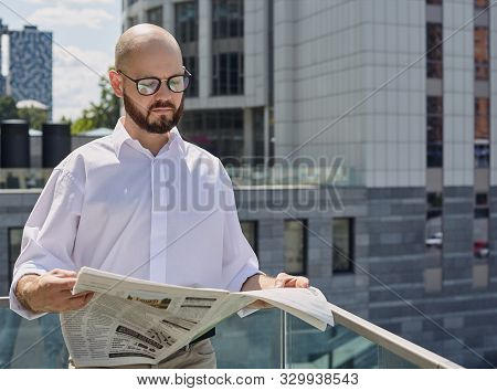 A Bald Guy With A Brown Beard And Pc Glasses Striped Shirt And Beige Pants With Laptop Sitting On Th