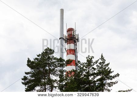 Red White Chimney With Steel Installation On Top Among Trees In Blue Sky Backdrop