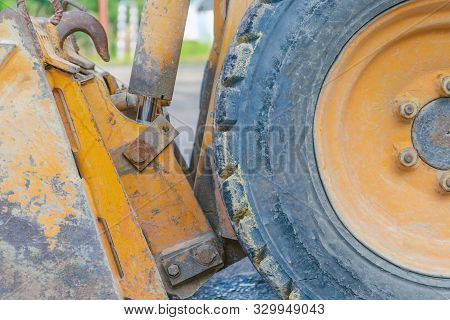 Scratched Metal Bucket Of A Small Old Orange Tractor. Old Tractor Wheel. Road Construction, Repair C