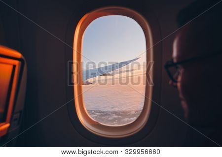 Man Looking Throught Vindow Of Airplane During Flight Above Clouds At Sunset. Selective Focus On Win
