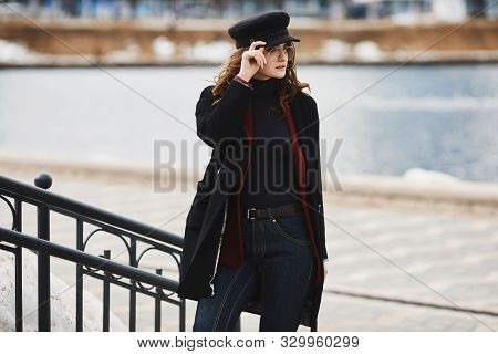 Fashionable Model Girl In A Coat, Modish Hat, And Sunglasses Posing Over An Urban Background. Beauti