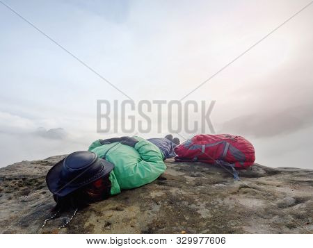 Woman Tourist Lays On Top Of The Word Above Heavy Clouds And Dreams. Hiker Wear Green Jacket And Lea