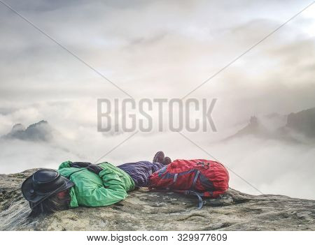 Woman Tourist Lays On Top Of The Word Above Heavy Clouds And Dreams. Hiker Wear Green Jacket And Lea