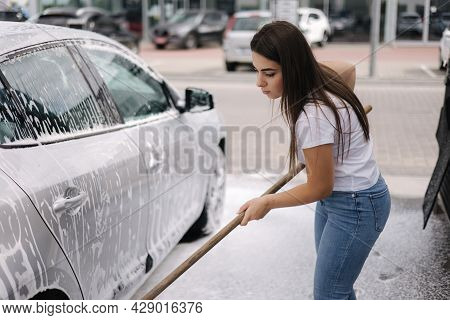 Attractive Young Woman Washing Her Car With Shampoo And Brushes. Female Washes Automobile With Foam 