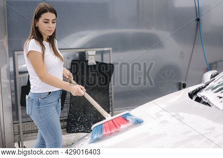 Attractive Young Woman Washing Her Car With Shampoo And Brushes. Female Washes Automobile With Foam 