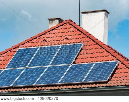 Solar Electric Panels Installed On The Red Tiled Roof Of A House  Europe. Modern Roof  Against The B