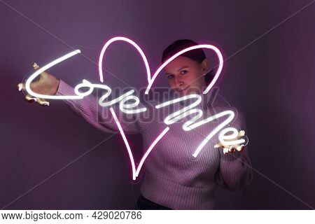 Beautiful Girl With Neon Signs. White And Pink Neon Heart With The Inscription Love Me. Trendy Style