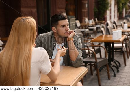 Man Getting Bored During First Date With Overtalkative Young Woman At Outdoor Cafe