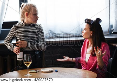 Alcoholism in family problem. Daughter aguring with her mother about drinking wine. Two people, woman and teenage girl quarrel in the kitchen. A depressed female is addicted to alcohol at home.