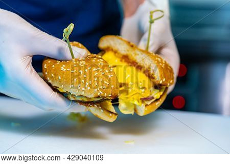 Cutted In A Half Tasty Appetizing Cheesburger. Chef In Gloves Showing A Hamburger With Meat Cutlet A