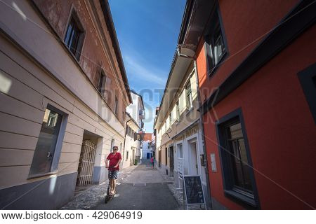 Kranj, Slovenia - June 15, 2021: Man Riding An Electric Scooter Driving In A Narrow Street Of Staro 