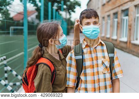 schoolboy and schoolgirl posing on the way to school, wearing a protective mask on their faces from a coronavirus infection, education and back to school concept