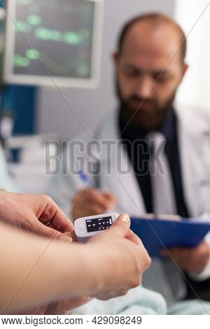 Asisstant Nurse Puts Medical Oximeter On Finger While Doctor Man Writes Heartbeat Puls Rate On Clipb