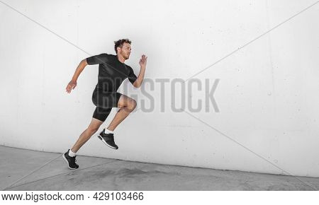 Sport athlete training running fast with explosive sprint for competition. Man runner working out at fitness gym outdoor white wall background.