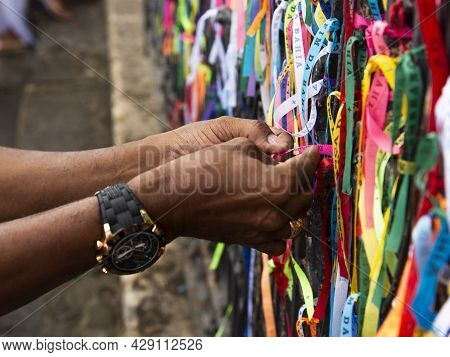 Hands Tying The Ribbons Of Senhor Do Bonfim On The Iron Railing.