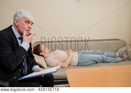 Caucasian Woman Lies On A Couch At A Reception With A Psychotherapist. An Elderly Man Works As A Psy