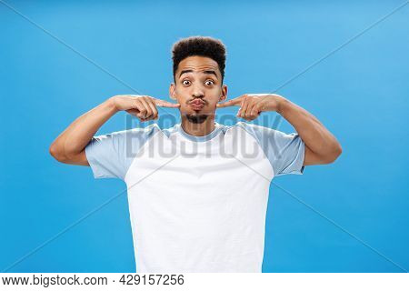 Waist-up Shot Of Playful Happy Nice African American Guy With Tattoo On Palm Holding Breath Pouting 