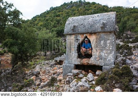 Hiking Lycian way. Tourist posing for photo inside Lycian rock tomb, stretch between Myra - Alakilise Ruins, Trekking in Turkey, outdoor activity, Ancient stone sarcophagus of Lycian necropolis