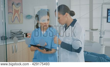 Dentist And Assistant Analyzing Modern Tablet Screen In Dental Cabinet. Stomatological Staff Using T