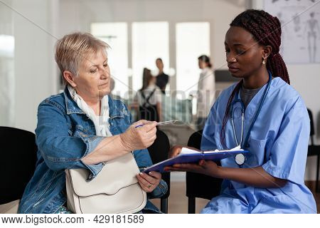 African American Nurse Explaining Sickness Treatment To Elderly Patient Putting Her To Sign Medical 