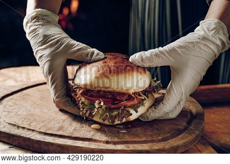 Gloved Hands Take A Hamburer From A Wooden Tray