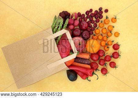Grocery shopping fruit and vegetables in a brown paper bag, high in lycopene for a healthy heart with immune boosting foods high in antioxidants, anthocyanins, vitamins, and fibre. On mottled yellow. 