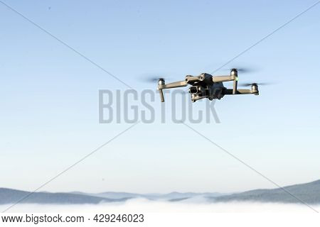 Drone Quadcopter Helicopter In The Air, In A Clear Blue Sky, Morning Fog And Mountains Below. Aerial