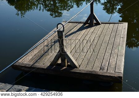 A Wooden Raft Is Tied To A Taut Rope. Self-service Ferry Across The River, Pond. People Get On And P