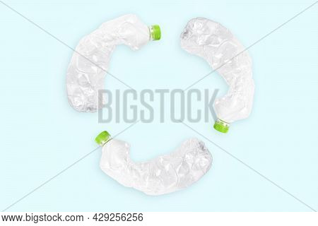 Three Crashed Plastic Bottles On Blue Background Form Resycling Sign. Plastic Utilisation Concept. A