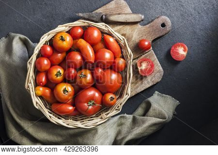 Fresh Red Tomatoes In Whicker Basket On Black Background. Flat Lay, Top View