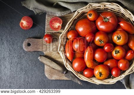 Fresh Red Tomatoes In Whicker Basket On Black Background. Flat Lay, Top View