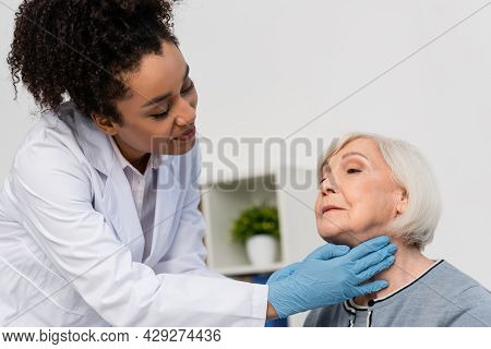 African American Docktor In While Coat Checking Neck Of Elderly Patient