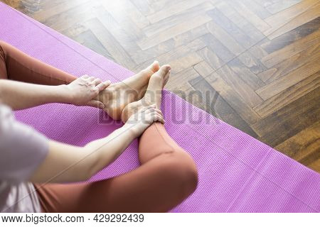 Young Woman In Sportswear Sitting On Youga Mat In Living Room And Doing Butterfly Stretch