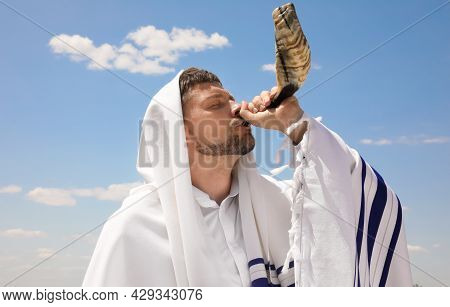Jewish Man In Tallit Blowing Shofar Outdoors. Rosh Hashanah Celebration