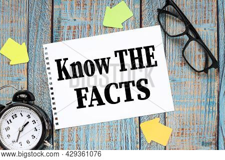 Know The Facts. On A Blue Wooden Table A Sheet Of Notepad. Table Clock And Glasses In Black