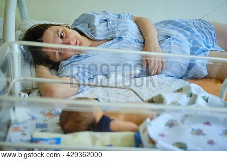 Mom Is Sleeping In The Ward With A Newborn Baby, A Maternity Hospital Bracelet On Her Arm. A Newly B