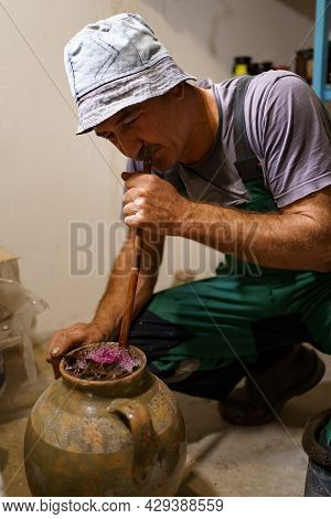 Man Making Pickles In A Ceramic Vasel Using An Old Recipy. He Enriches The Contents Of The Vessel Wi