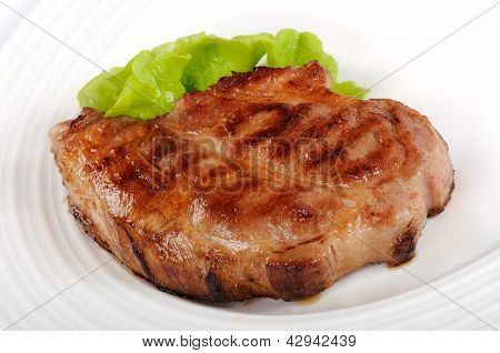 Gegrilltes Schweinesteak auf einem weiÃŸen Teller mit grÃ¼nem Salat