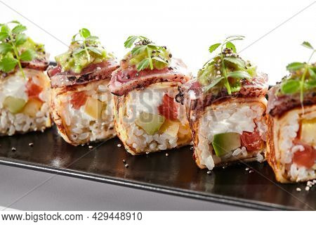 Japanese sushi roll with japanese omelette - tamagoyaki. Sushi roll with avocado and cream cheese inside, topped with fried tuna. Delicious sushi roll with fish topped with sauce and fresh greens