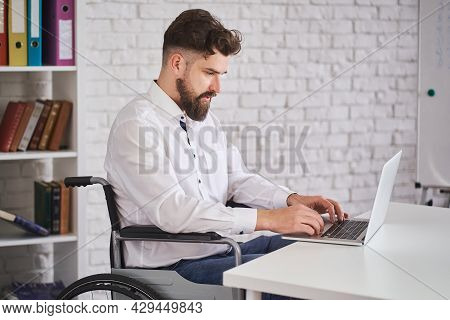 Concetrated Office Employee Sitting On A Wheelchair And Working On A Laptop