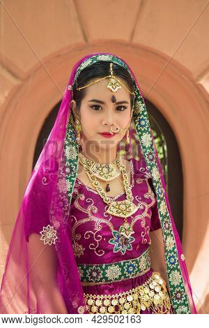 Portrait Asian Woman In A Margenta Indian Tradition Sari, She Is Looking At A Camera With Orange Wal