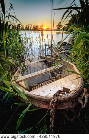 Old Iron Rowing Boat Sunk Half Way On The Waterfront Of A Pond At Sunset