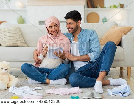 Preparing For Childbirth. Pregnant Muslim Couple Making Checklist Of Baby Things Before Going To Mat